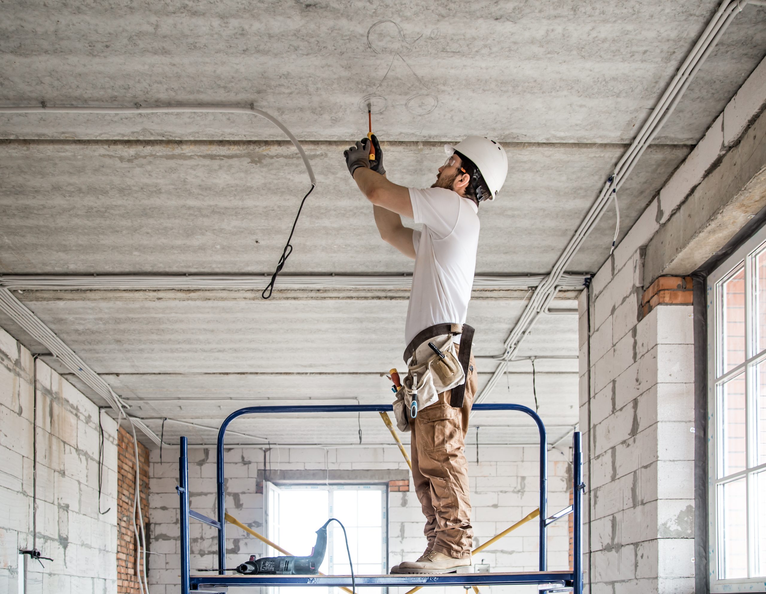 Electrician installer with a tool in his hands, working with cable on the construction site.